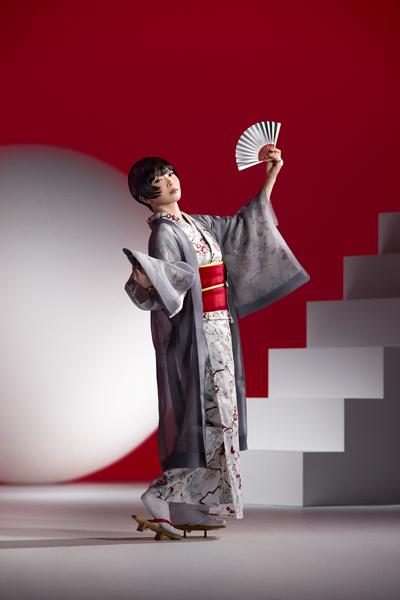 Figure in a grey kimono holding a white fan before a large red circle